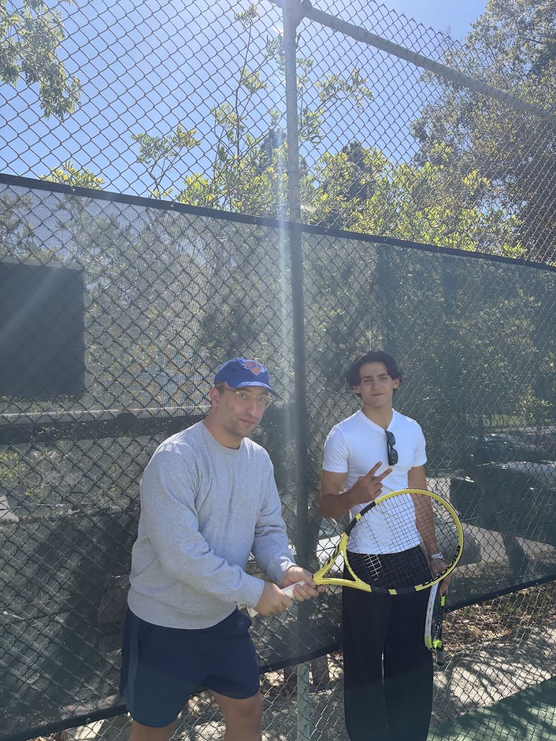 Two players by the fence, one holding a racquet.