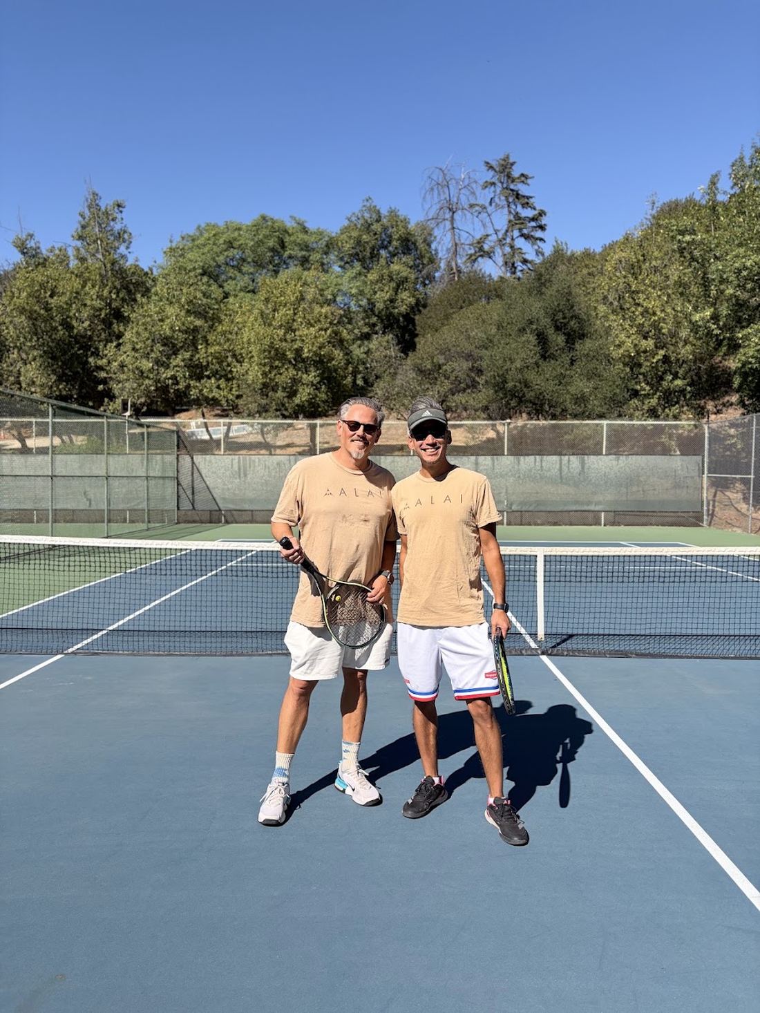 Two players in ALAi shirts at the net after a game.