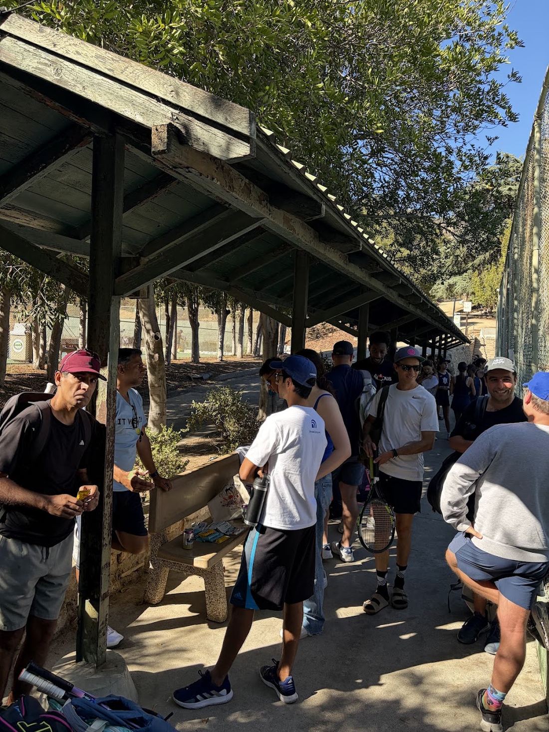 Players gathered in the shade by the lower courts with drinks and snacks.